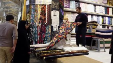 Dükkan sahibi, Şiraz, İran 'da bir kumaş dükkanındaki müşterilere renkli kumaş cıvatalarını gösteren bir platformda duruyor.