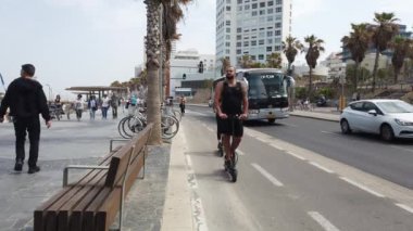 Turistler ve yerliler güneşli bir bahar gününün tadını çıkarıyorlar Tel Aviv, İsrail 'deki sahil gezisinde elektrikli scooterlara binip geziyorlar.