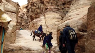Eşeklerin yanında yürüyen ve ata binen turistler antik Petra, Ürdün 'de bir patikadan aşağı iniyorlar.