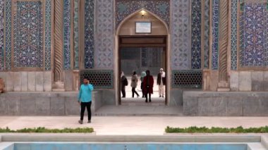 Kırmızılı kadın Kerman, İran 'daki Ganjali Camii' nden çıkarken, bir adam yakındaki bir cep telefonuyla konuşuyor.