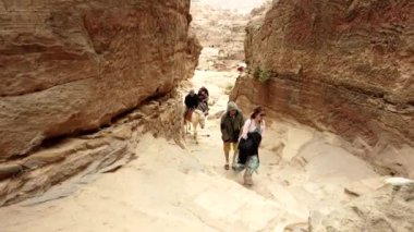 Turistler Petra, Jordan, bazıları yürüyüş, bazıları binek eşekleriyle Siq 'e doğru ilerliyorlar.