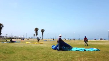 Eğitmen kumsalın yakınındaki çimenli bir arazide güneşli bir yaz gününün tadını çıkararak yamaç paraşütü açıyor.