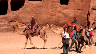 Turistler, Petra, Ürdün 'deki hazinenin yakınındaki deve yolculuğunun keyfini çıkarıyorlar.