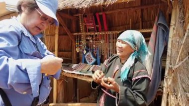 Geleneksel giysili bir kadın, canlı bir pazar yerinde bir müşterisiyle alışveriş yapıyor.