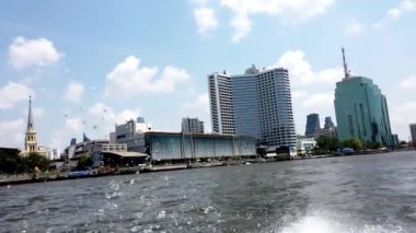 Bir sürat teknesi, Bangkok 'taki Chao Reynaya nehri kıyısındaki modern otellerin yanından geçerken su sıçrıyor.