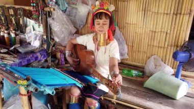 Karen kabilesinden geleneksel boyunluk takan bir kadın gitar çalıyor, kültürel mirasını ve zanaatkarlığını sergiliyor.