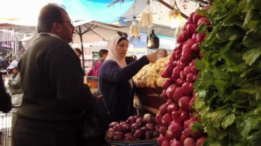 Başörtüsü takan bir kadın markette soğan seçerken kocası onu ilgiyle izliyor.