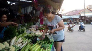 Taylandlı gri tişörtlü satıcı Sukhothai, Tayland 'daki açık hava pazarında müşterilere taze sebze paketliyor.