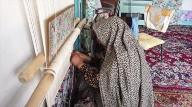 Yaşlı zanaatkar kadın, İsfahan, İran 'daki atölyesinde geleneksel İran halısı örüyor ve hünerini sergiliyor.