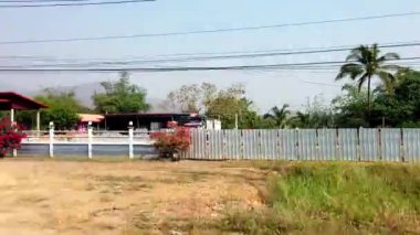 Tren pirinç tarlalarını, Budist tapınağını, muz ağaçlarını ve kırsal Tayland evlerini geçerek sakin kırsal bölgeleri gösteriyor.