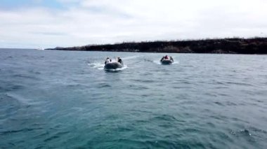 Galapagos adalarından birini ziyaret ettikten sonra turistlerle dolu iki bot ana tur teknesine dönüyor.