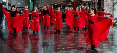 Halka açık bir alanda canlı kırmızı elbiseler içinde zarif dans eden bir grup kadın.