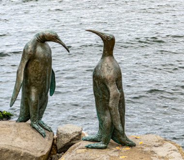 Artistic metal sculptures of two penguins in a conversational pose by a riverside clipart