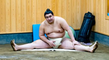 Sumo wrestler takes a breather, sitting on the floor after a tough training session clipart