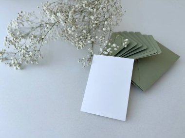 Davetiye ya da tebrik kartı modeli zeytin zarfları ve doğal beyaz çigila çiçekleri, kopyalama alanı. Çiçekli, beyaz, boş düğün davetiyesi.