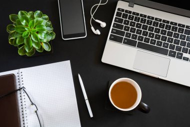 Top view of workplace with laptop, notebook with pen and other items on black desktop. Flat lay