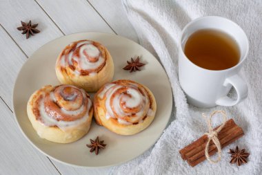 A plate with delicious cinnamon rolls and a cup of tea on a white wooden table