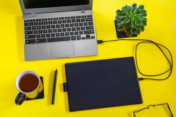 Graphic designer workplace: laptop with graphic tablet on desktop with yellow surface