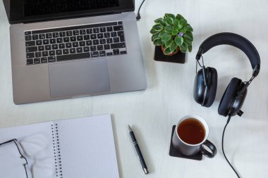 Beyaz masaüstünde dizüstü bilgisayarı, not defteri ve bir fincan çayı olan işyeri