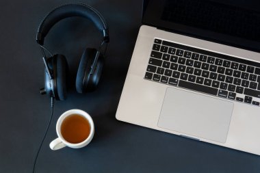 Bilgisayarlı, kulaklıklı ve siyah masaüstünde bir fincan çay olan bir iş yeri.