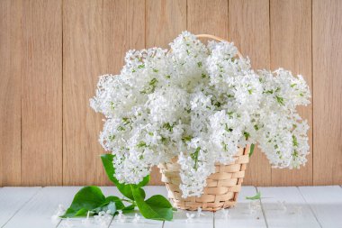 Tahta bir masanın üzerinde hasır sepetin içinde beyaz leylaklar.