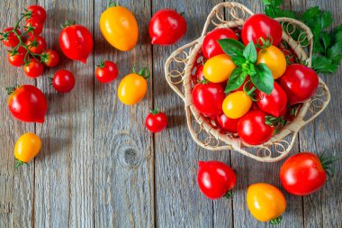 Tahta bir masada hasır bir tabakta taze kırmızı ve sarı domatesler.