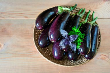 Tahta arka planda hasır bir kasede taze taze patlıcanlar.