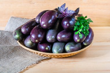 Tahta arka planda hasır bir kasede taze taze patlıcanlar.