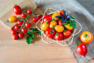 Tahta bir masada hasır bir kasede kırmızı ve sarı olgun domatesler.
