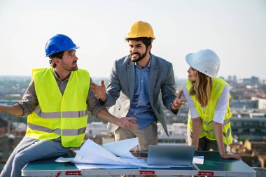 Mimarlar ekibi inşaat sahasındaki grup halinde belgeleri ve iş akışını kontrol ediyor.