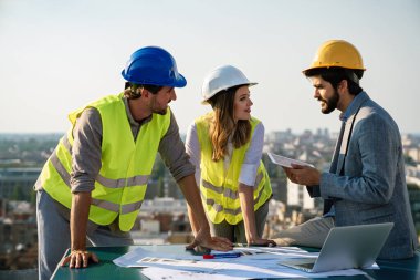 Mimarlar ekibi inşaat sahasındaki grup halinde belgeleri ve iş akışını kontrol ediyor.