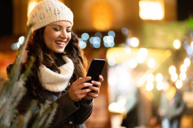 Genç ve güzel bir kadın, bir kış gününde cep telefonunu internette akıllı telefonuyla geziyor. İnsanlar teknoloji mutluluk kavramı