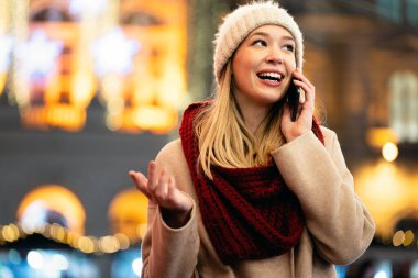 Kışın sokakta akıllı telefon kullanan gülümseyen güzel bir kadının portresi. İnsanlar alışveriş teknolojisi konsepti ile seyahat eder