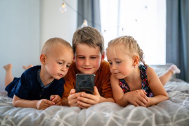 Evde birlikte cep telefonuyla oynayan çocukların portresi. İnternet ve ağ bağımlılığı.