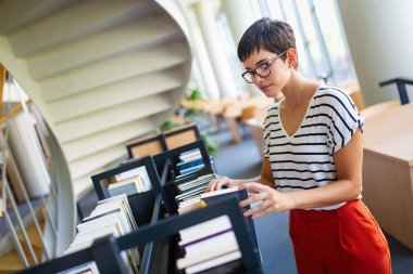 Eğitim kütüphanesi, üniversite eğitimi ve insanların konsepti. Üniversite kütüphanesinde kitap okuyan gülümseyen öğrenci kız.