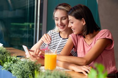 İki güzel kadının portresi. Eğleniyorlar, birlikte telefon kullanıyorlar ve kafede sohbet ediyorlar. İnsanlar mutluluk teknolojisi konsepti