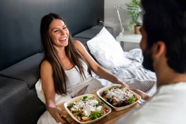 Güzel, genç, romantik bir erkek, bir kadına yatakta kahvaltı getirir ve uyandıktan sonra birlikte güler..