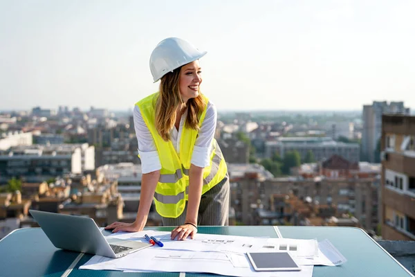 Young successful woman construction specialist architect reviewing blueprints at construction site