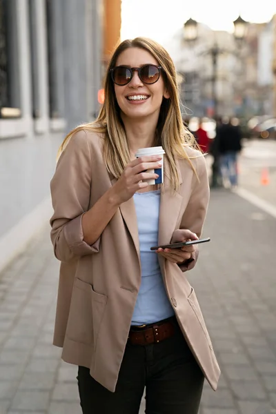 Attractive young successful woman drinking a coffee and using a smartphone while enjoying break