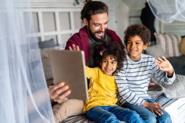 Mutlu baba ve çocuklar dijital tablet kullanıyor ve evde eğleniyorlar. Çok ırklı aile mutluluğu kavramı