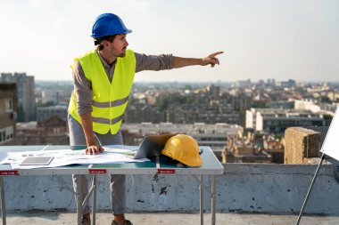 Genç başarılı inşaat şantiyesi mühendisi inşaat sahasının mimari planlarıyla çalışıyor..