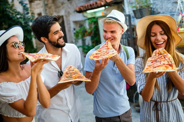 Happy group of friends eating pizza while traveling on vacation