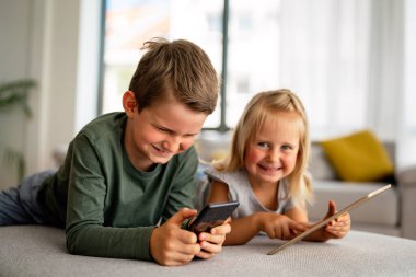 Akıllı telefonlu küçük çocukların portresi evde oyun, çocuk ve cihaz konsepti oynuyorlar.