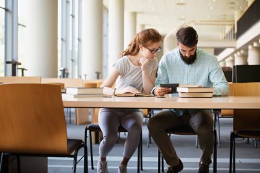 Kütüphanede kitaplarla çalışan mutlu genç üniversite öğrencileri. Üniversitede bir grup çok ırklı insan