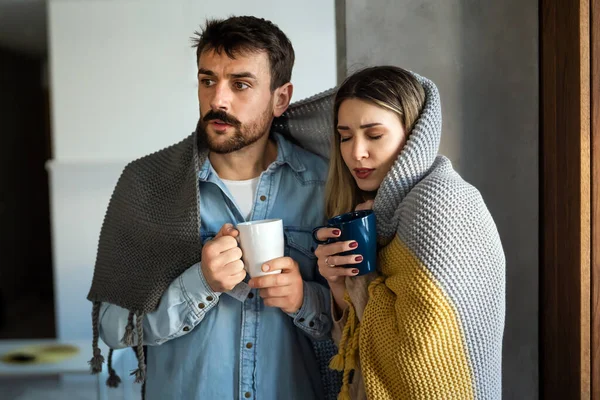 悲伤的年轻夫妇裹在毯子里 喝着热茶 试图取暖 冻结患感冒或流感发烧或中央暖气问题的男女 — 图库照片