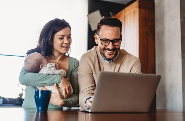 stock image Portrait of young happy couple with a baby at home, using laptop. Father is trying to work from home.