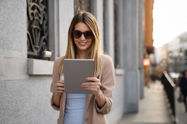 Dijital tablet kullanan başarılı bir genç kadının portresi kentsel arkaplanda kısa bir mola sırasında