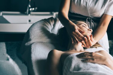 Masör spa salonunda genç kadın vücuduna masaj yapıyor.