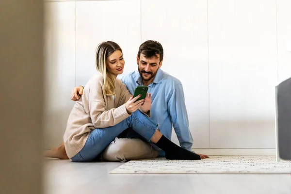 年轻夫妇通过电话在家里分享社交媒体新闻 微笑着在网上购物 移动技术生活方式概念 — 图库照片