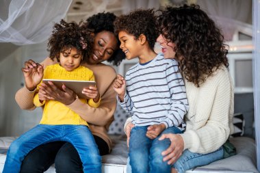 Mutlu çoklu etnik aile dijital cihazlarla eğleniyor. Homoseksüel ebeveynler ve küçük çocuklar dijital tablet kullanıyorlar..